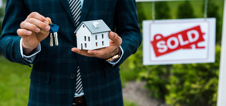 Hands holding a small model of a house adn a set of keys